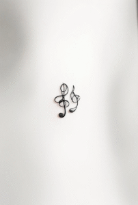 simple music tattoo featuring tiny heart, note, and treble clef symbols in minimalist black line style