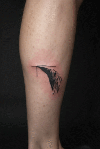 “Minimal cliff edge line tattoo on the side of a man’s calf, created with thin black lines to represent risk and courage.”