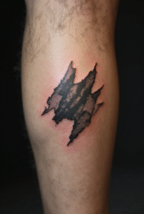 “Tiny torn paper tattoo on the outer male calf, outlined with thin jagged lines to symbolize unfinished stories and growth.”