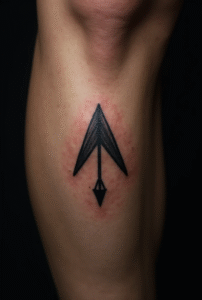 “Close-up of a tiny Spartan arrowhead tattoo on a male calf, designed with sharp minimalist black lines symbolizing courage and discipline.”